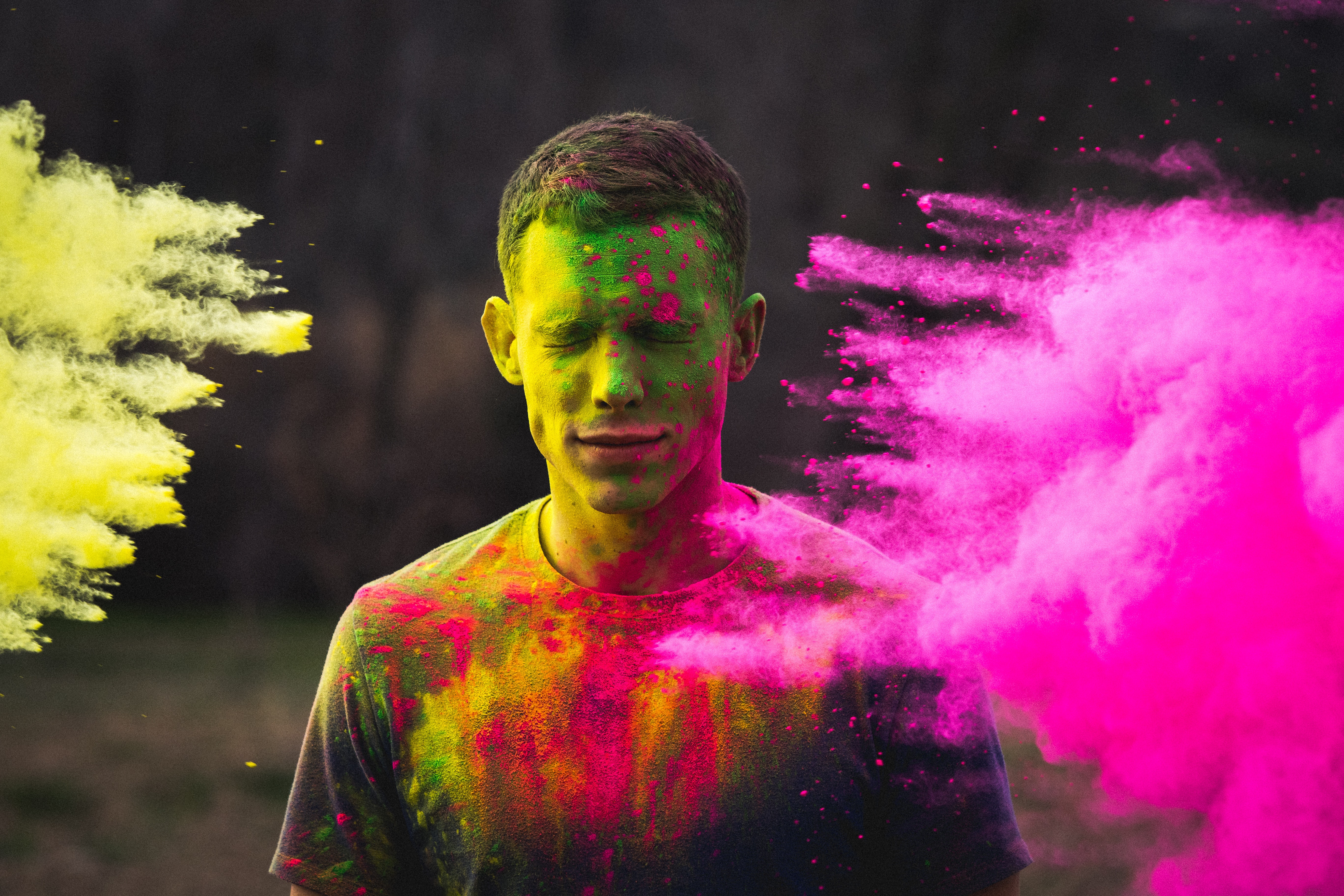 A man with his eyes closed being splashed with paint. A pink paint cloud appears on the right.