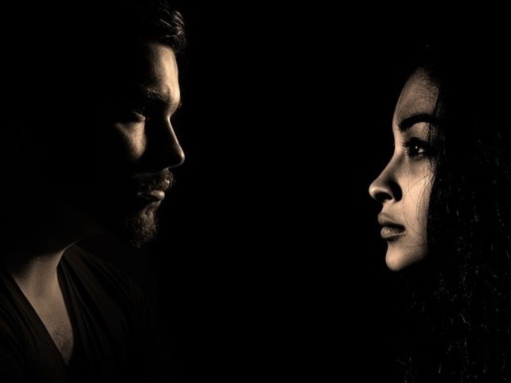 A dark picture of a man and a woman facing each other with their faces illuminated