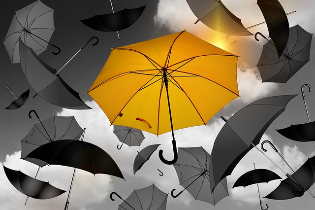 A yellow umbrella standing out from a bunch of black and gray umbrellas