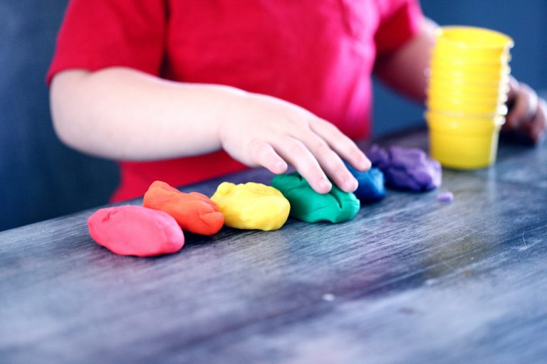 young child lining up playdough in the colors of the rainbow from red to violet.