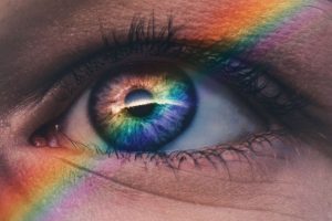 Picture of a person's eye close up with a rainbow going over it in a diagonal line. The iris of the eye blends into the color of the rainbow overlaying it.