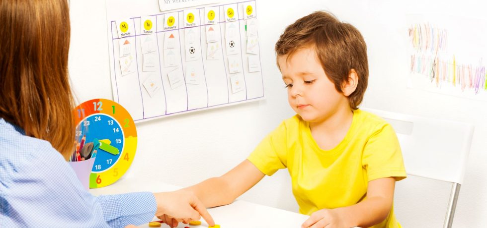 Therapist white woman pointing to an object on a table and a white boy pointing to another object on the table.