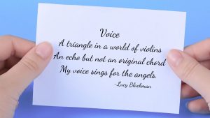 A card in a person's hand against a blue background. On the card is a poem from Lucy Blackman titled, Voice. The poem read: A triangle in a world of violins, an echo not an original chord, my voice sings for the angels.