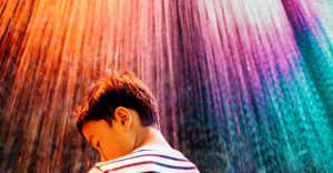 A young boy with autism faces an abstract wall of rainbow colors