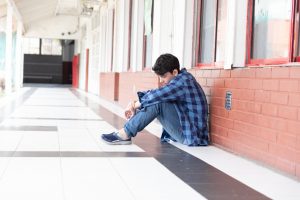 A boy leans against a hall in school, looking sad and alone. To represent autism asperger's autistic on the spectrum in the classroom and school environment. It goes with the poem poetry in this story.