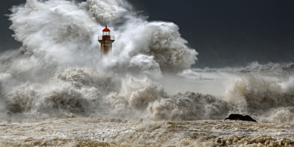 Image of a lighthouse in a storm about to be covered by a wave. Image is a metaphor for how an autistic person with autism may feel during a meltdown